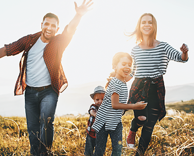 Fotografía de una mujer, un hombre, una niña y un niño. Los cuatro sonríen mientras corren hacia la cámara.